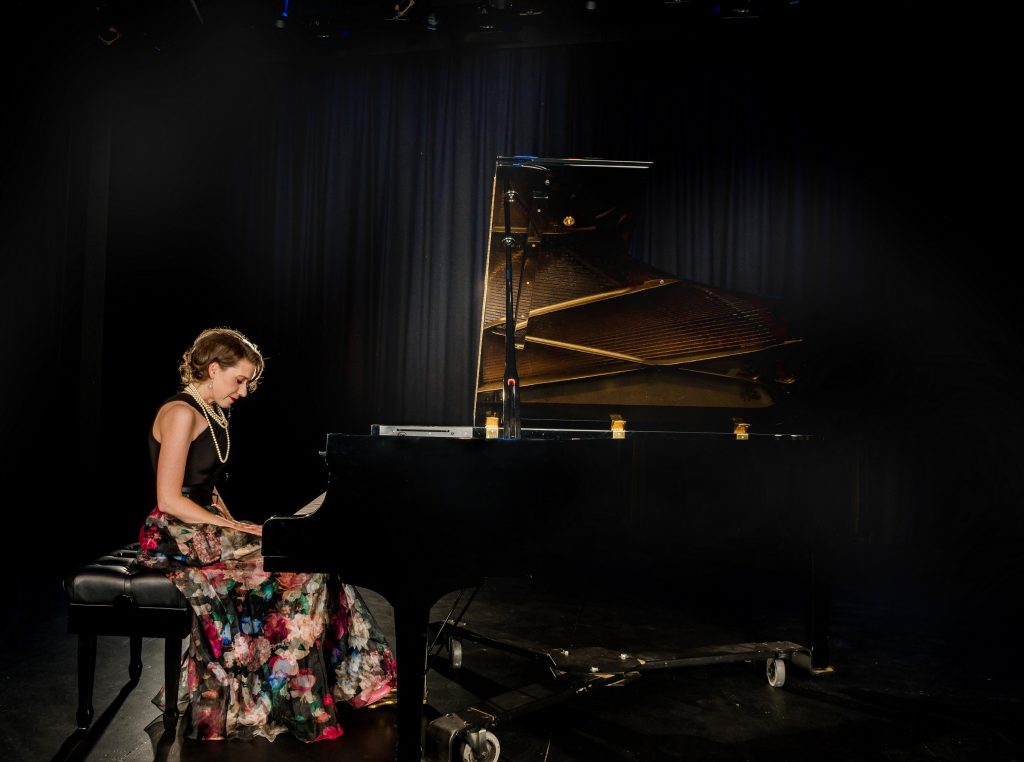 Sara Hagen sitting at a piano on a dark stage