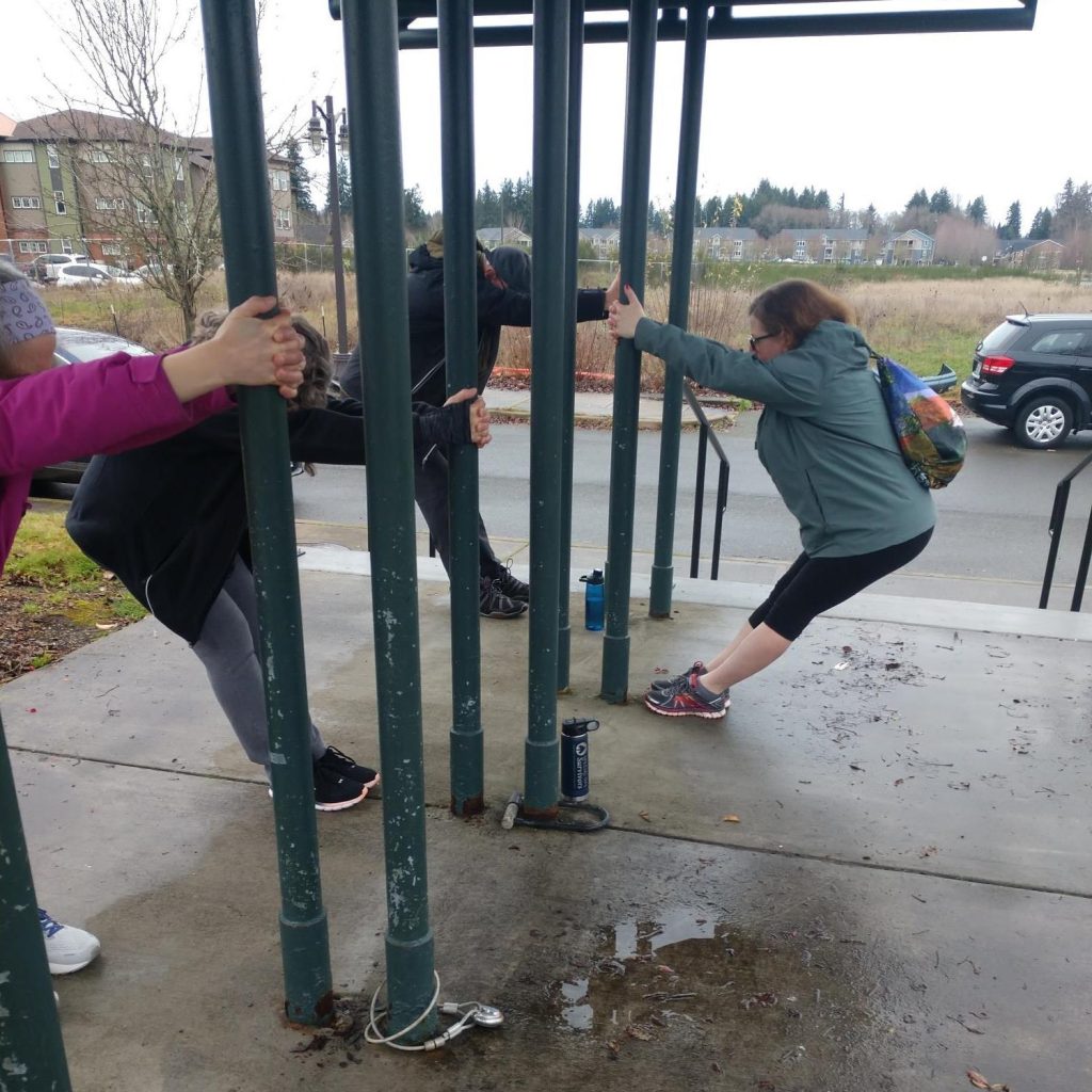 people with their hands wrapped around poles, stretching away from it with their feet up against them.