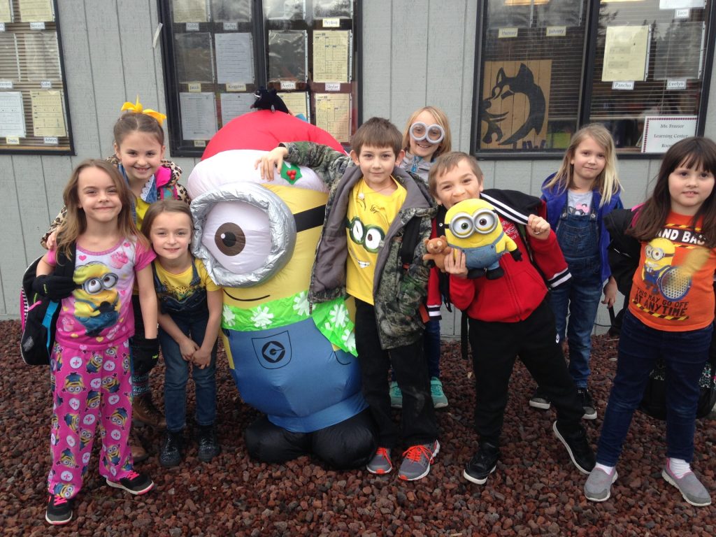 a group of grade school dies with minion clothes and a stuffed minion, pose for a photo with a blow up minion.