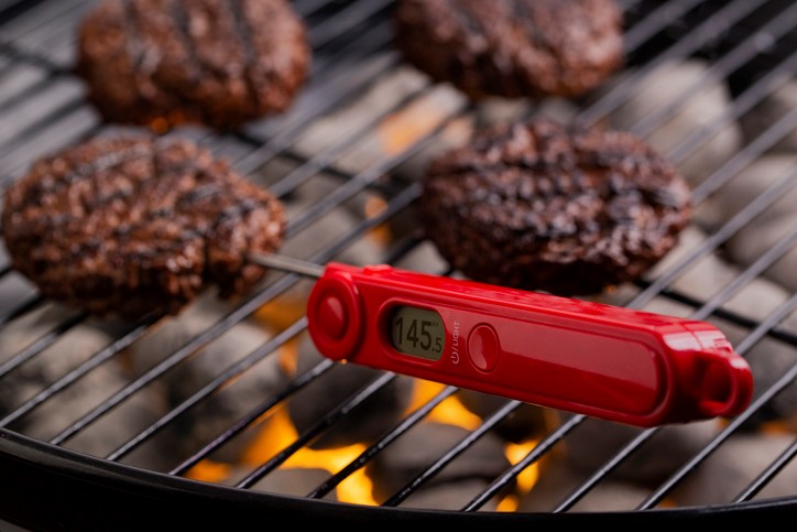 a red food thermometer inside a burger patty on a grill with the temper '145' on it.
