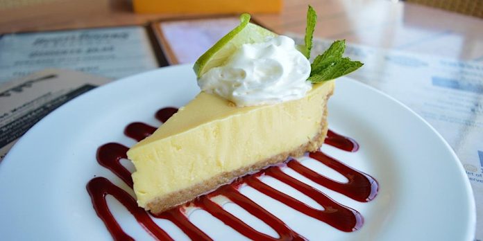 a slice of cheesecake with whipped cream and raspberry drizzle on a white plate