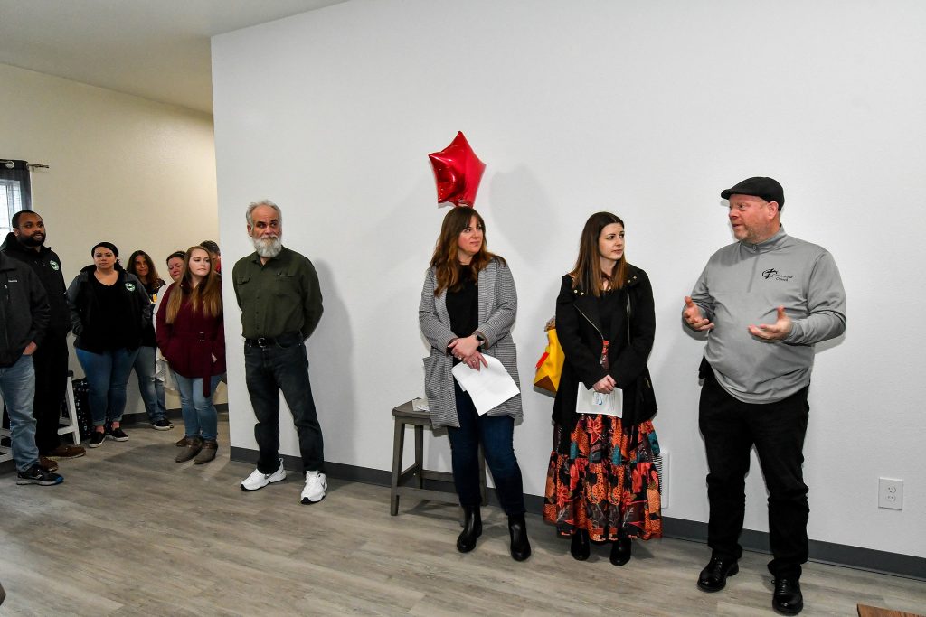 People standing in a room listening to a man next to them talk, a red star balloon is on a chair