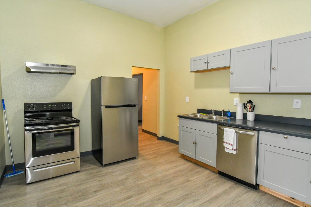 a small kitchen with freestanding range, fridge and a small counter with a dishwasher and cabinets above it