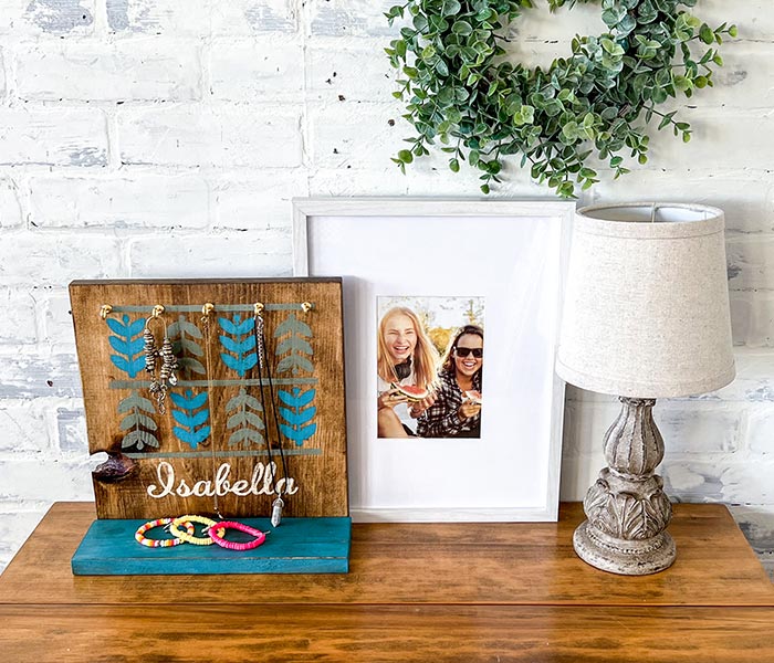 a decorated wood jewelry holder with jewelry on it, a photo in a frame and a white lamp on a wooden table