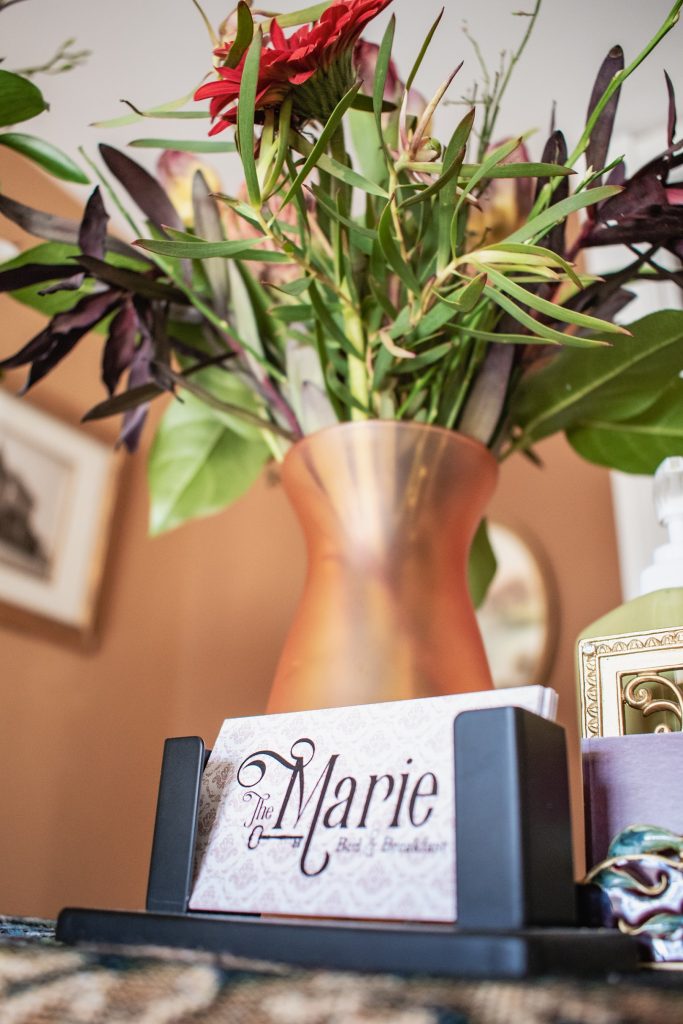 close up of The Marie Bed & breakfast business cards sitting under an orange vase filled with flowers