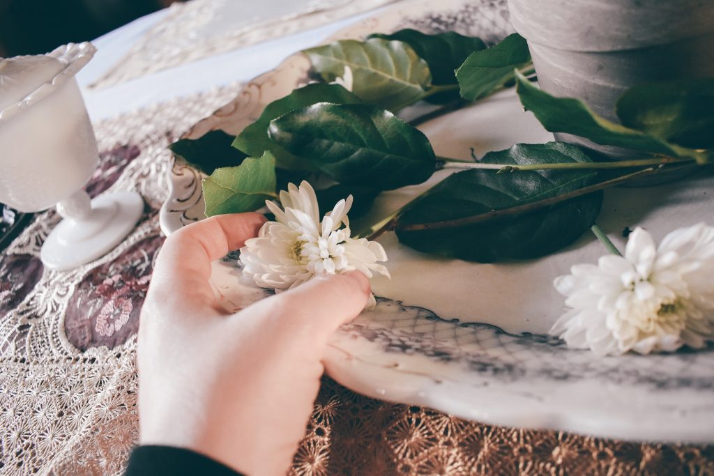 a hand places flowers on a china dish sittin on a lace tablecloth