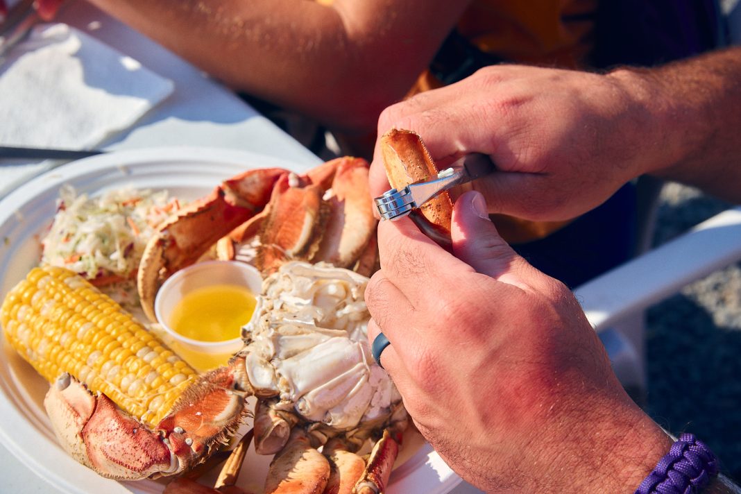 two hands cracking open a crab leg over a plate with a crab, corn and potatoes on it