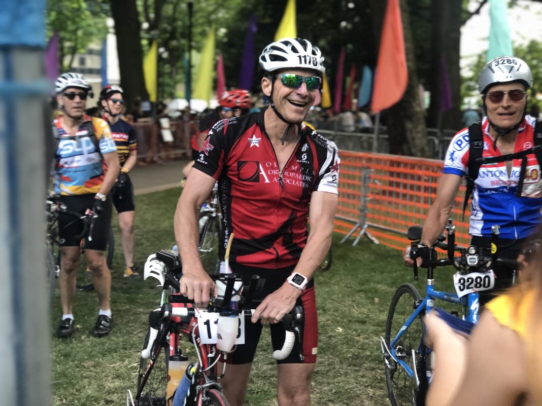 Tom Helpenstell standing next to his bike, other bike riders with their bikes are around him