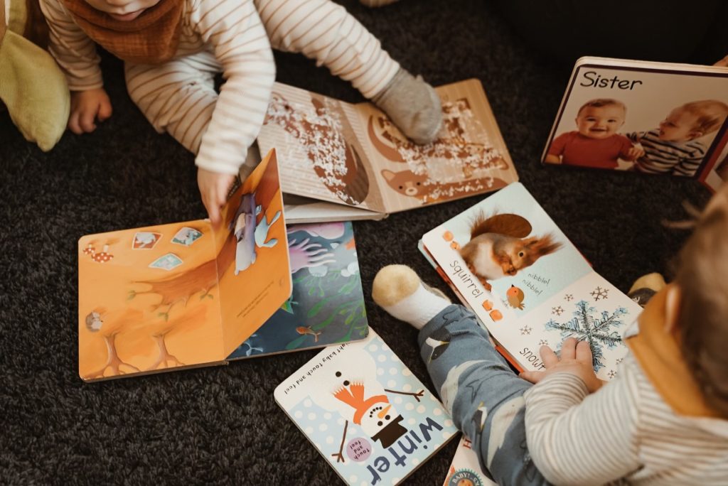two infants sitting on the floor with picture books