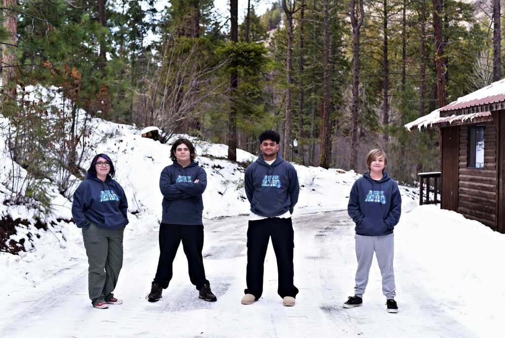 four youth standing in the snow outside a log cabin
