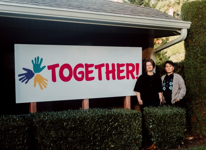 Sierra Abrams (left) and Kahlo C. Flores M. (right). standing by a white sign with three handprints on it and the word, 'TOGETHER!'