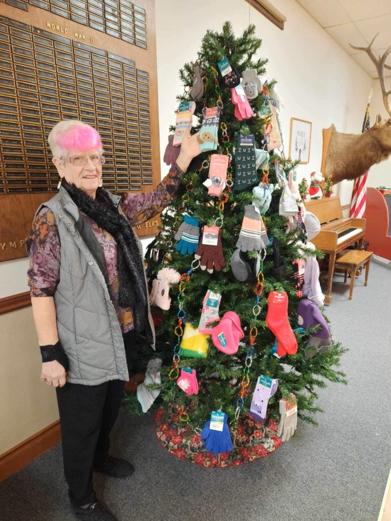 a woman puts socks on a Christmas tree covered in socks and mittens.