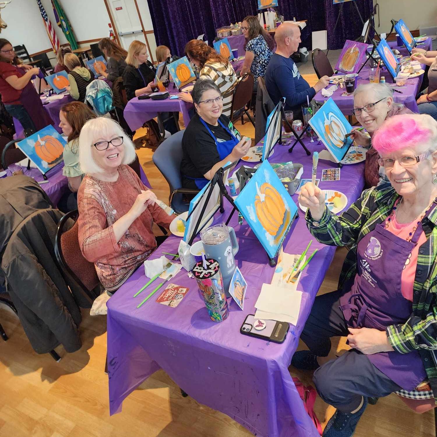 Olympia Elks members sitting at long tables painting a pumpkin portrait and sipping drinks.