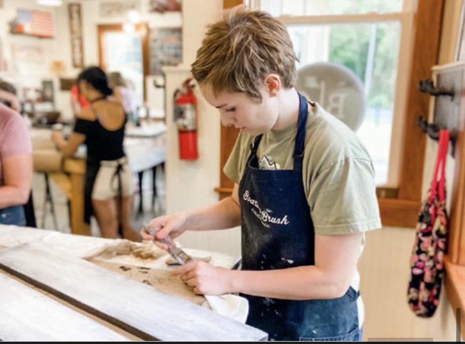 a youth wearing an apron stands at a table and wood works