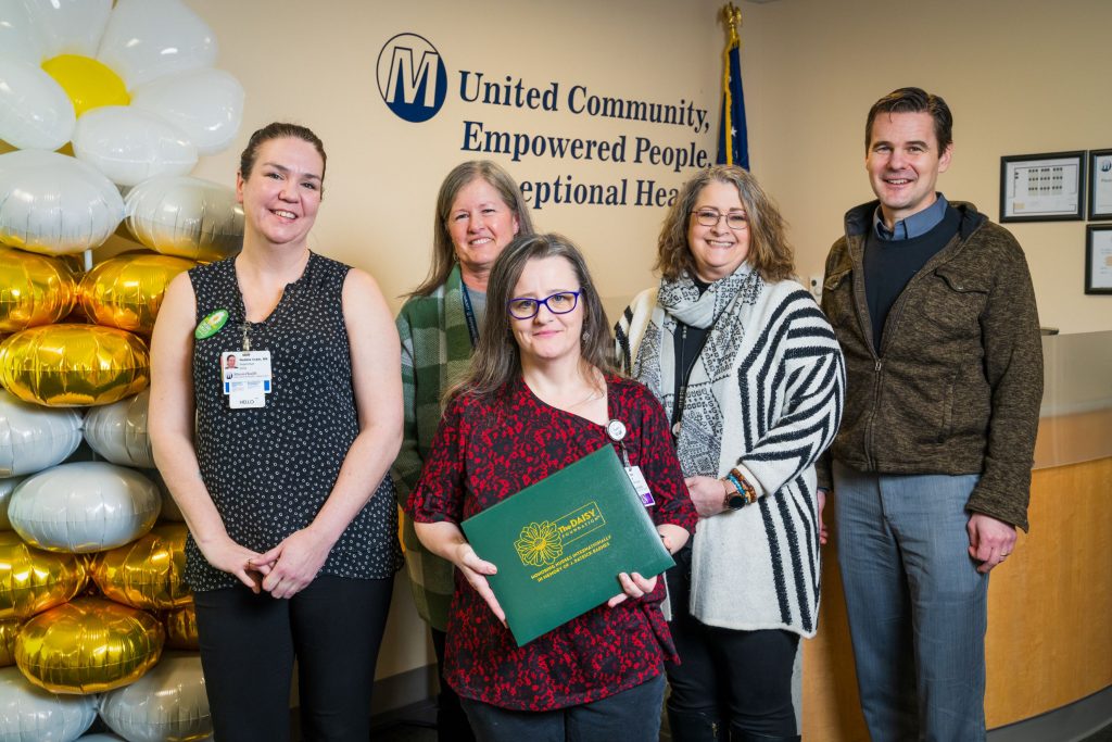group of Mason Health employees posing for a photo, one in the center is holding a green leather award folder