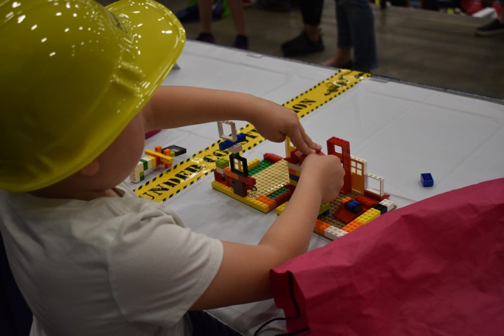 a kid in a yellow hard hat playing with construction toys on a table