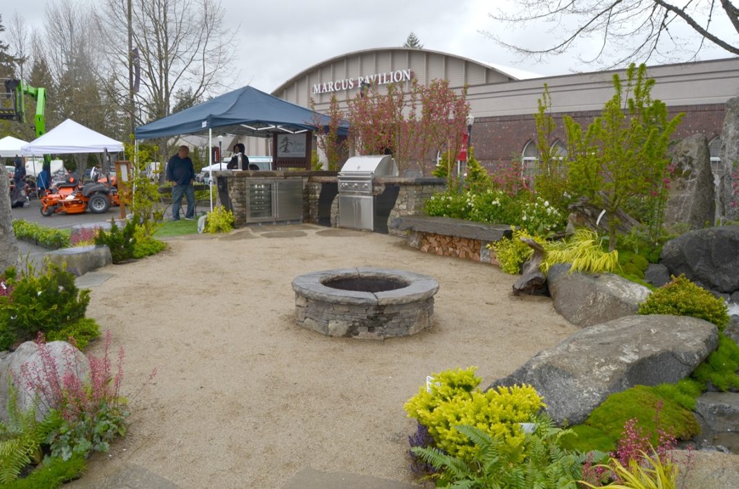 a landscape design example with a firepit and plant around it staged outside the Marcus Pavilion at Saint Martins for the Home and remodel show. Orange tractors are next to it.