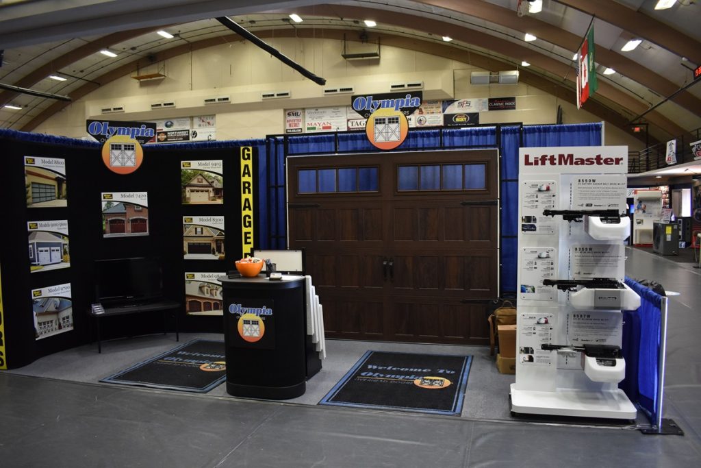 a garage door company's booth at a trade shoow with a garage door sample set up and photos of other samples next to it.