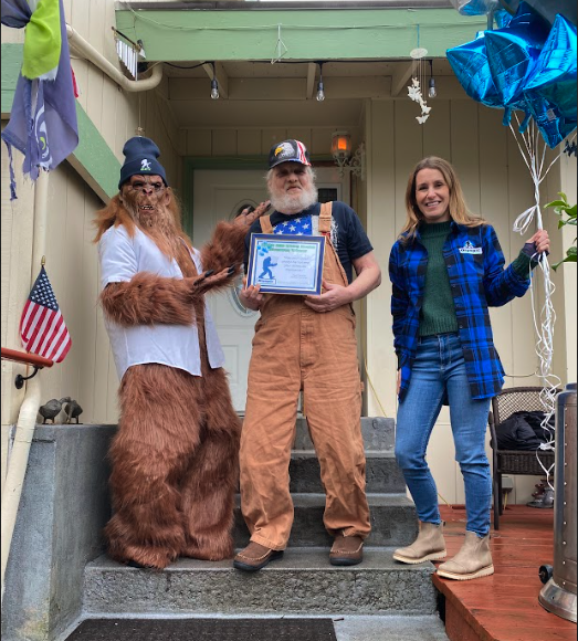 Kimberly Boeckman, a person dressed as a bigfoot and Kevin Hartley standing on a porch with balloons and donuts