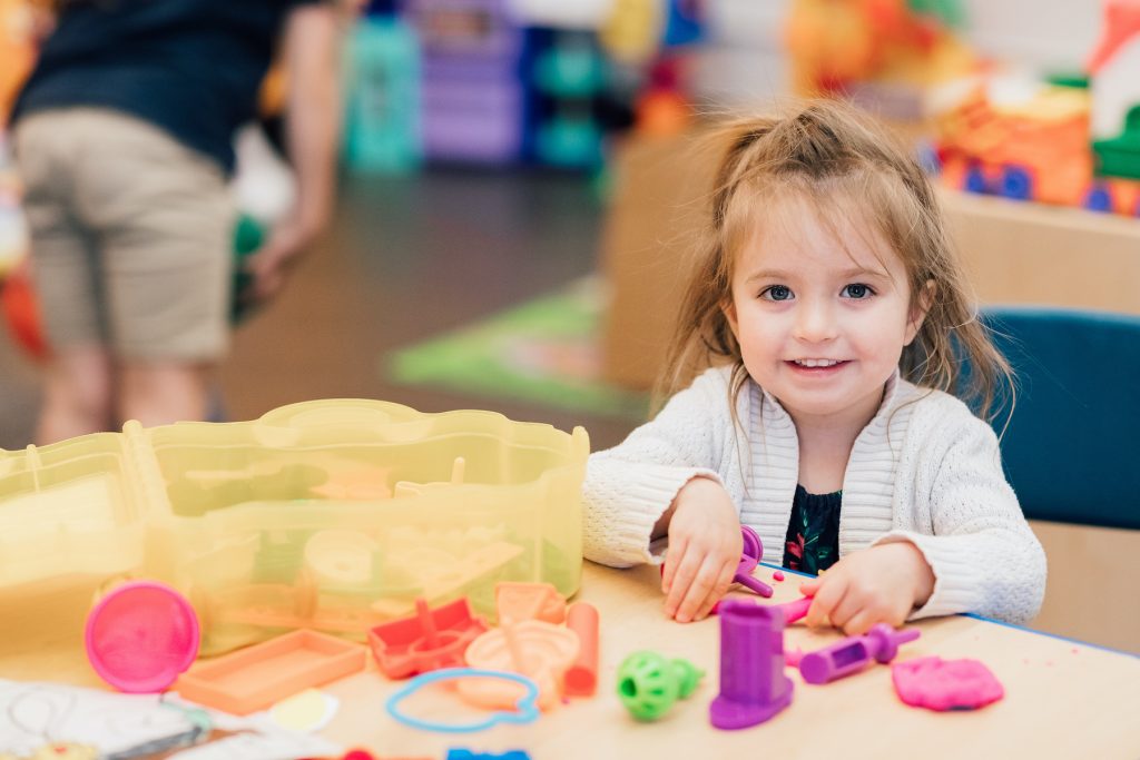 little girl sitting at a table playing with clay