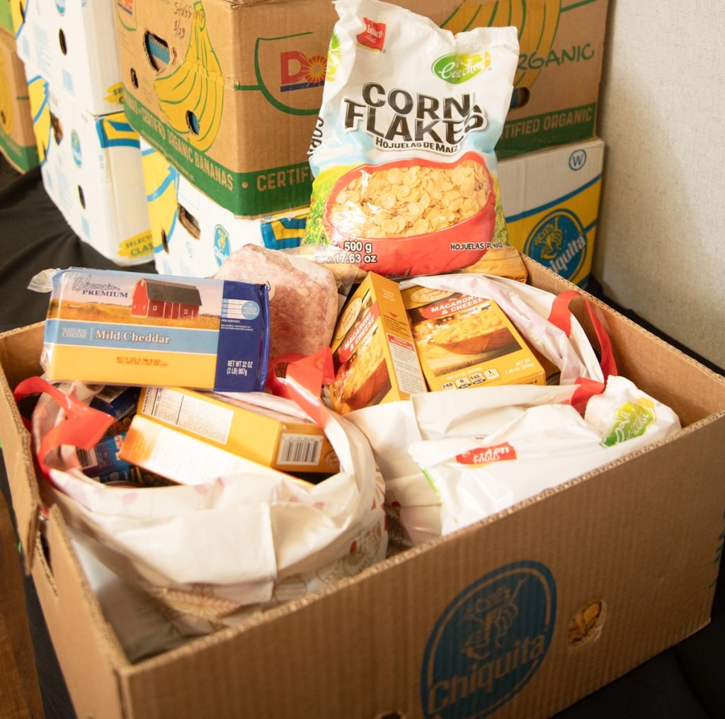 a cardboard box full of nonperishable food items, other boxes are stacked behind it
