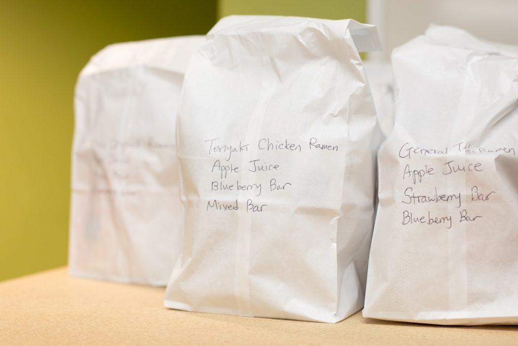 White paper bags with food items inside. Writing on outside of bag says what the contents are