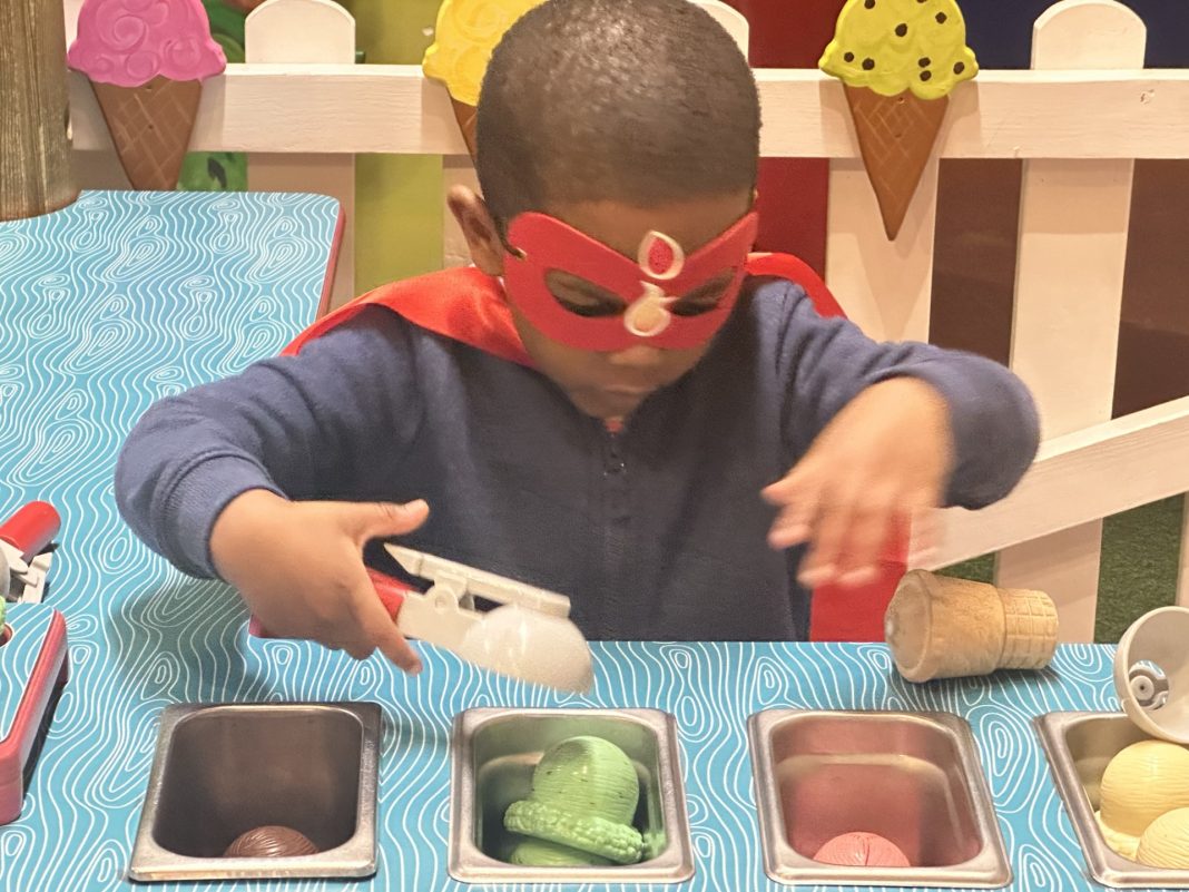 kid wearing an eye mask and a cape plays with plastic ice cream
