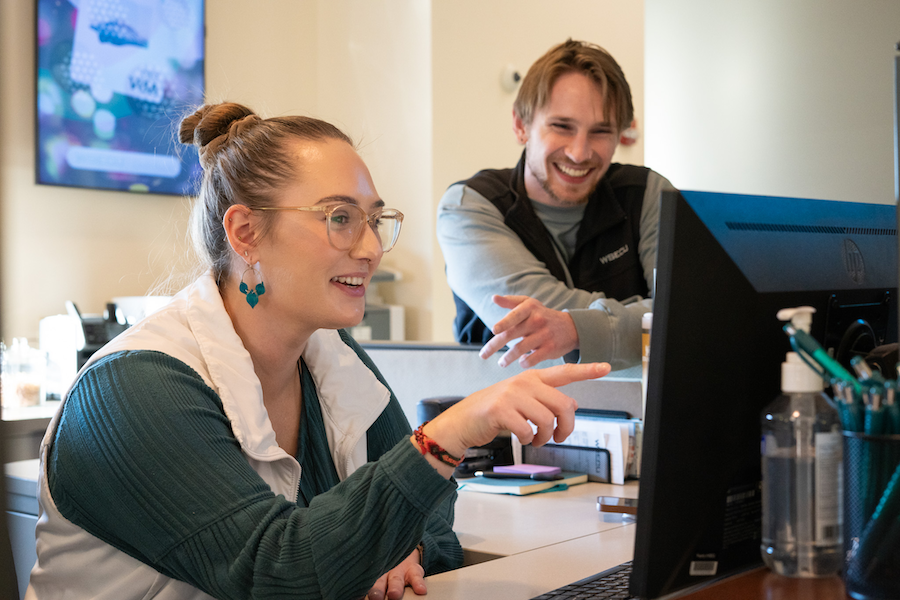 2 WSECU workers sitting at their desks looking at their computers and smiling