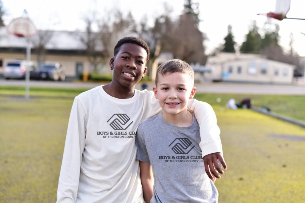 two kids, one with their arm over the other, standing in a field