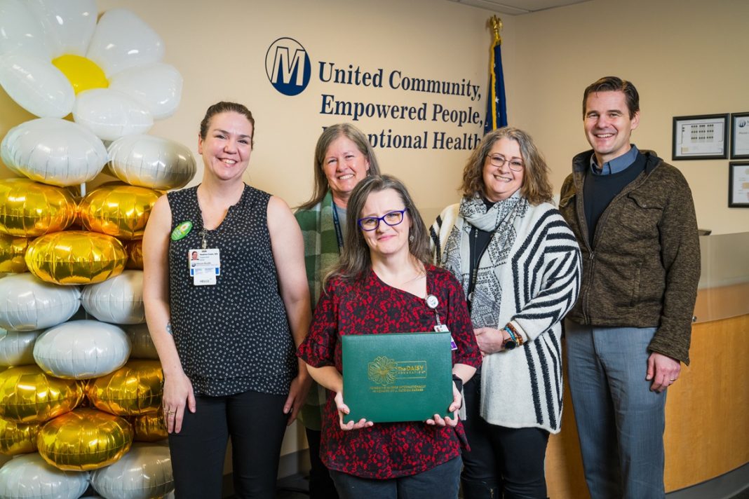 five people pose for a photo, the woman in the middle holds a green award folder