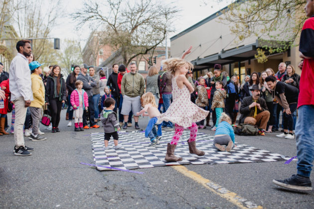 Kids dancing on a black-and-white checkered mat with a crowd around them on the street in downtown Olympia
