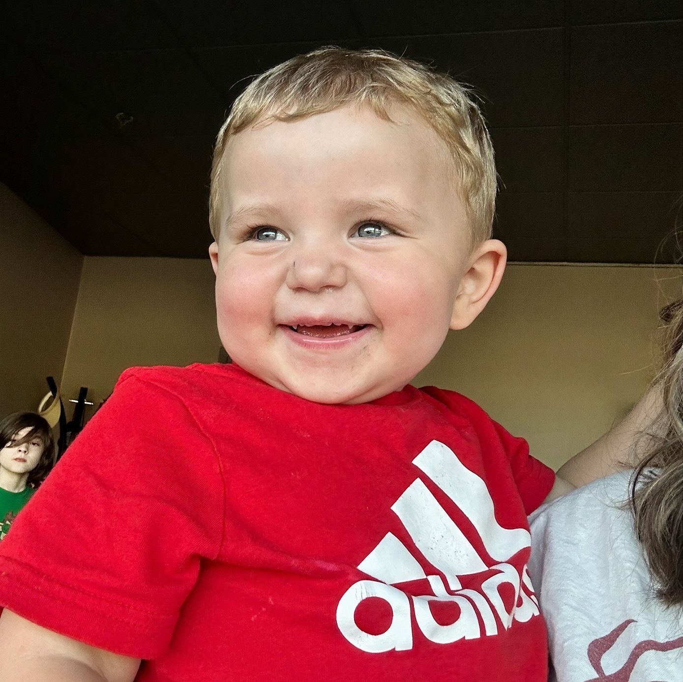 young boy in an Adidas t-shirt smiling while being held