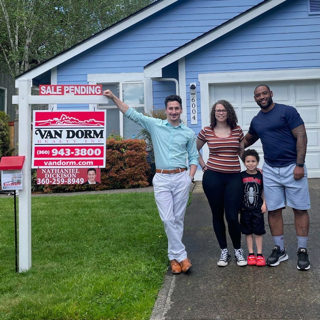 Nathaniel Dickison resting his hand on a Sale Pending Van Dorm Realty for sale sign with a woman, child and man standing next to him in front of a house