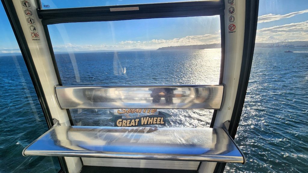 An empty seat on the Seattle Great Wheel with the water as the backdrop. A sole boat speeds by in the far back.