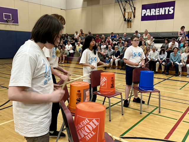 Kids in a school gym playing on 5-gallon plastic buckets