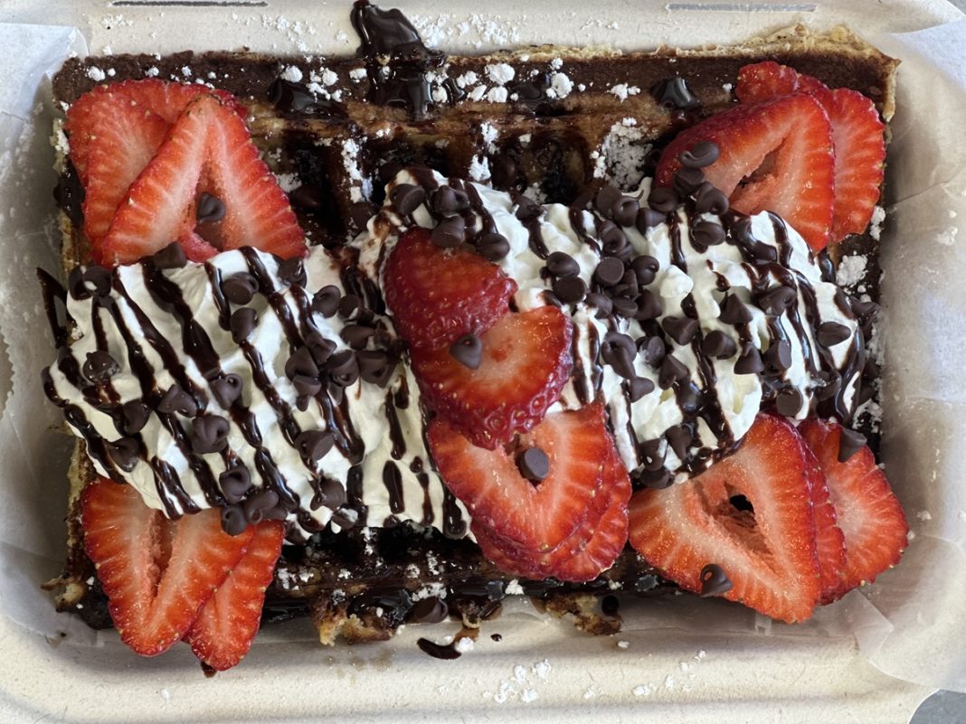 a waffle covered in strawberries, whipped cream and chocolate drizzle.
