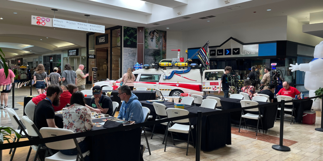 people at tables playing games, with the ghostbuster car in the background, inside Capital Mall