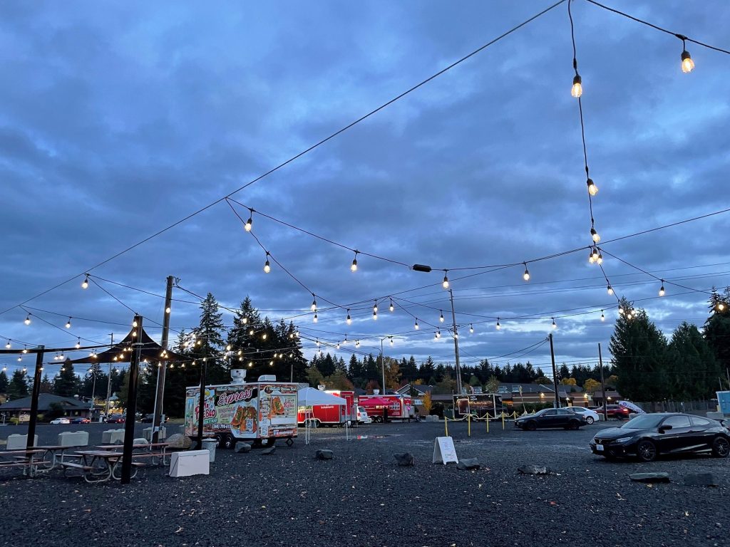 Food Trucks lined up in a gravel area at dusk with string lights overhead