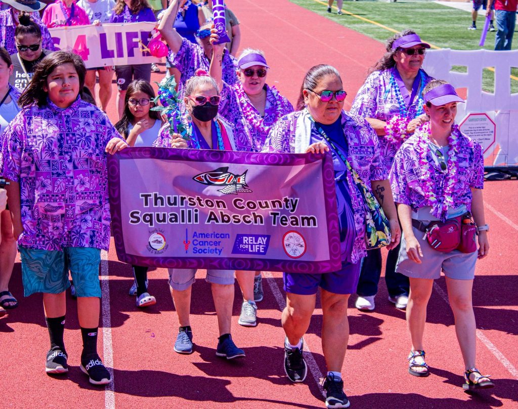 large group of people running on a track. Front people are holding a Relay for Life banner