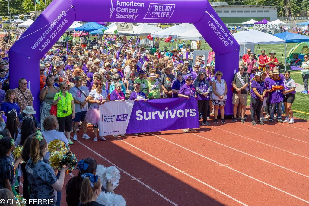 Huge crowd of people waiting to start a relay for life run under a large inflatable purple arch