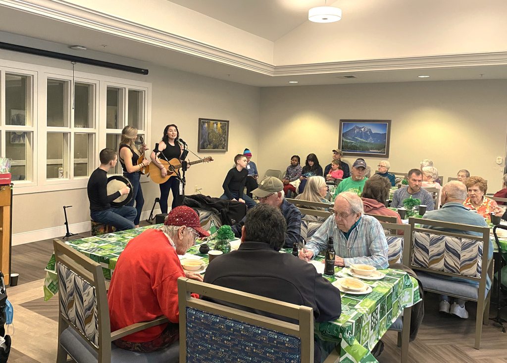 Senior citizens at long tables with St. Patrick's Day decorations eating Irish food and having bottles of Guiness