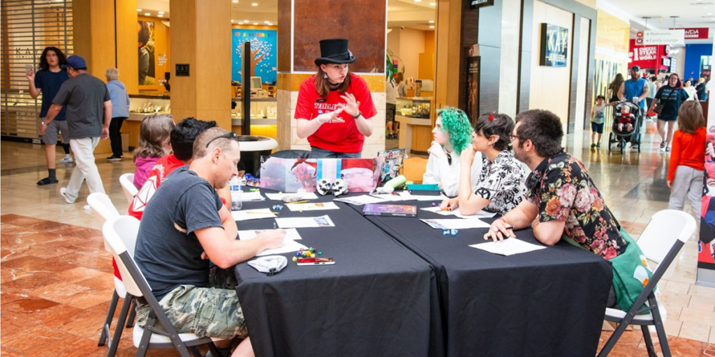 people sitting at a large table inside Capital Mall. They are dressed up and the person at the head of the table is standing up talking.