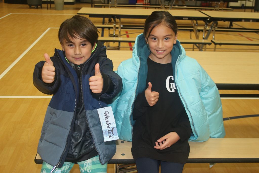 two kids pose with their new coats and give the camera a thumbs up.