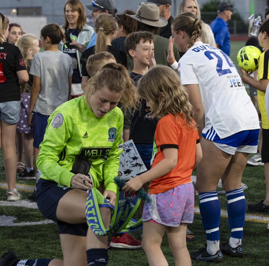 Olympia FC women soccer player kneeling down to sign something for a young fan