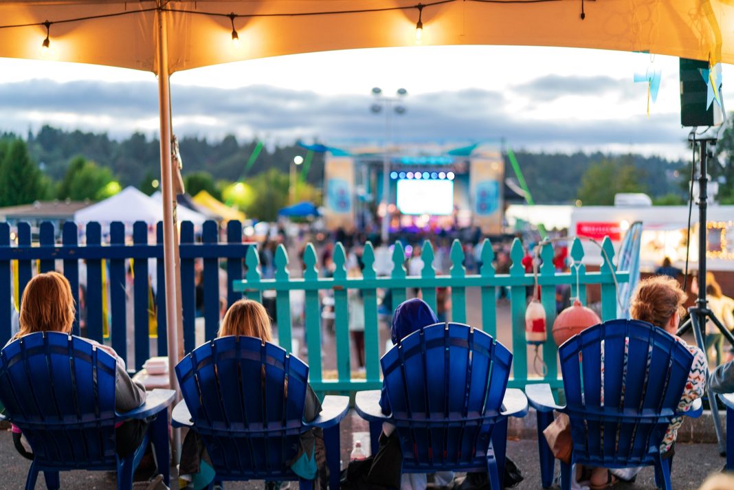 people sitting under a covered tent with a music festival in front of them
