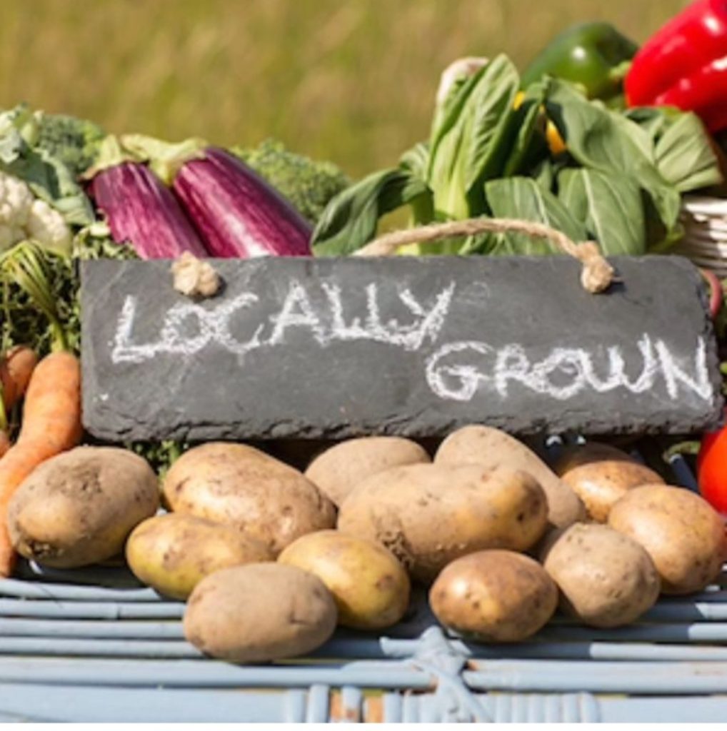 a pile of potatoes and vegetables with a chalkboard sign sitting on them that says, 'locally grown'