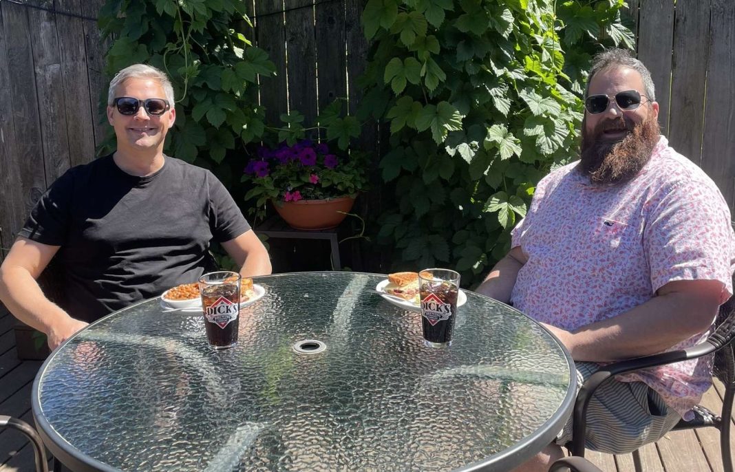 two guys sit at a glass round table with beer and food