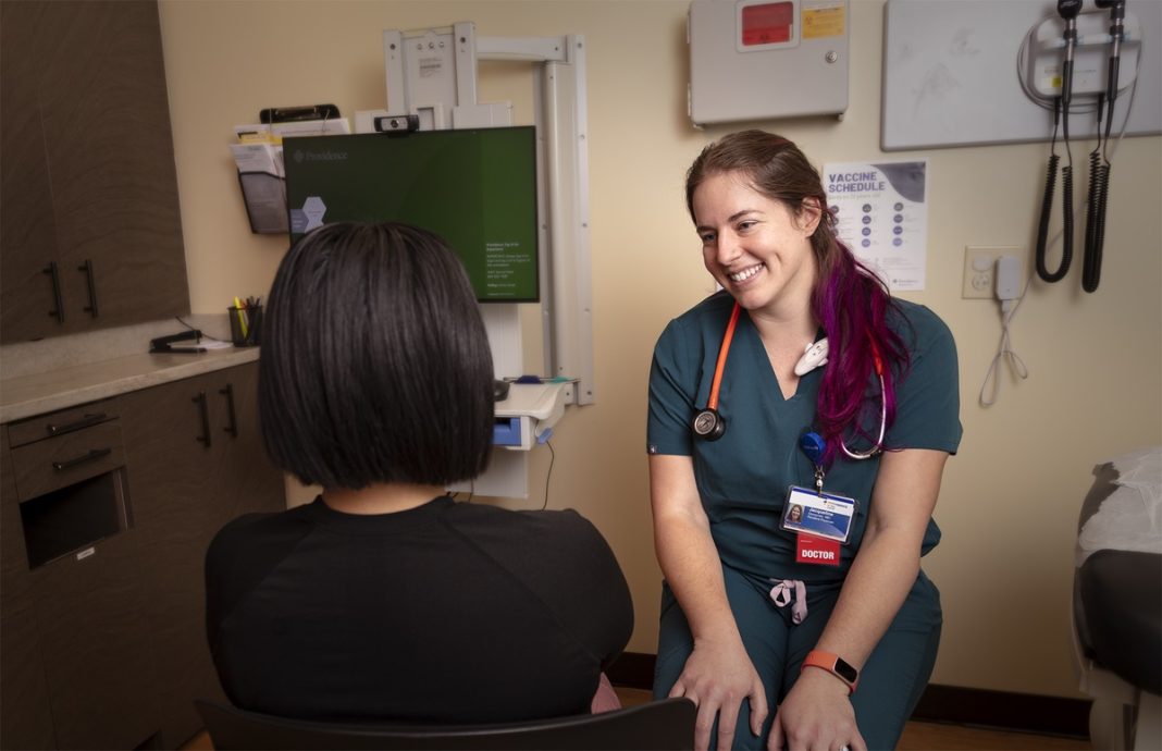 a female doctor smiling as she talks to a female patient, who is sitting with her back to camera