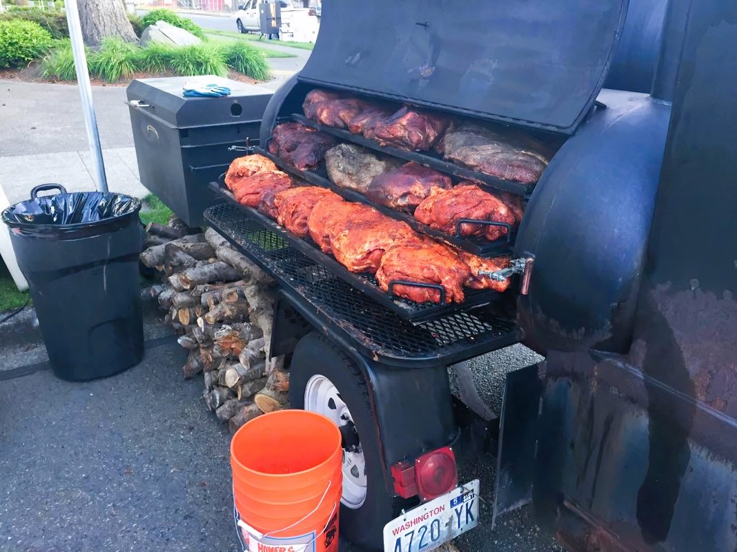 meat on a large black outdoor grill with wood stacked under it