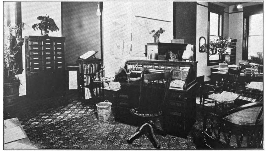 black and white photo of a desk covered in books and papers. A card catalog is next to it